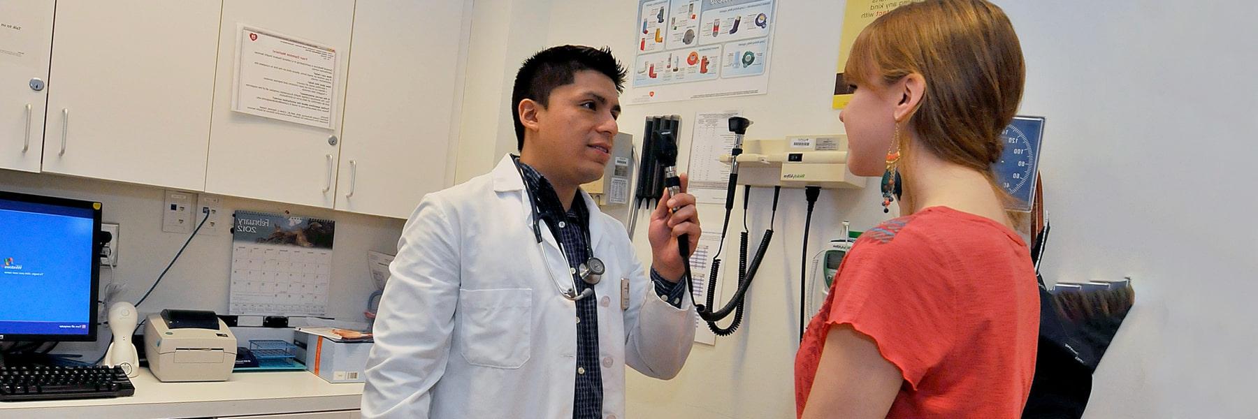 马塞诸斯州大学波士顿 staff member in white coat with stethoscope examines student sitting on a medical table